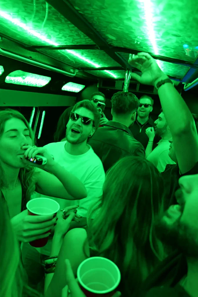 Friends with cups celebrating inside a party bus with green LED lights