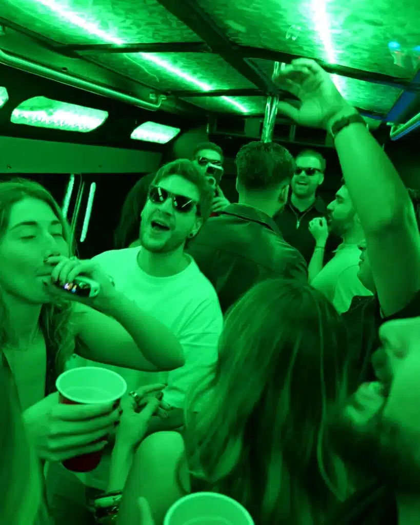 Friends with cups celebrating inside a party bus with green LED lights