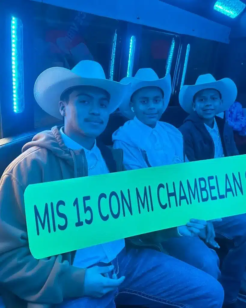 Quinceañera guests in cowboy hats holding a "Mis 15 con mi chambelán" sign inside a party bus with blue lights